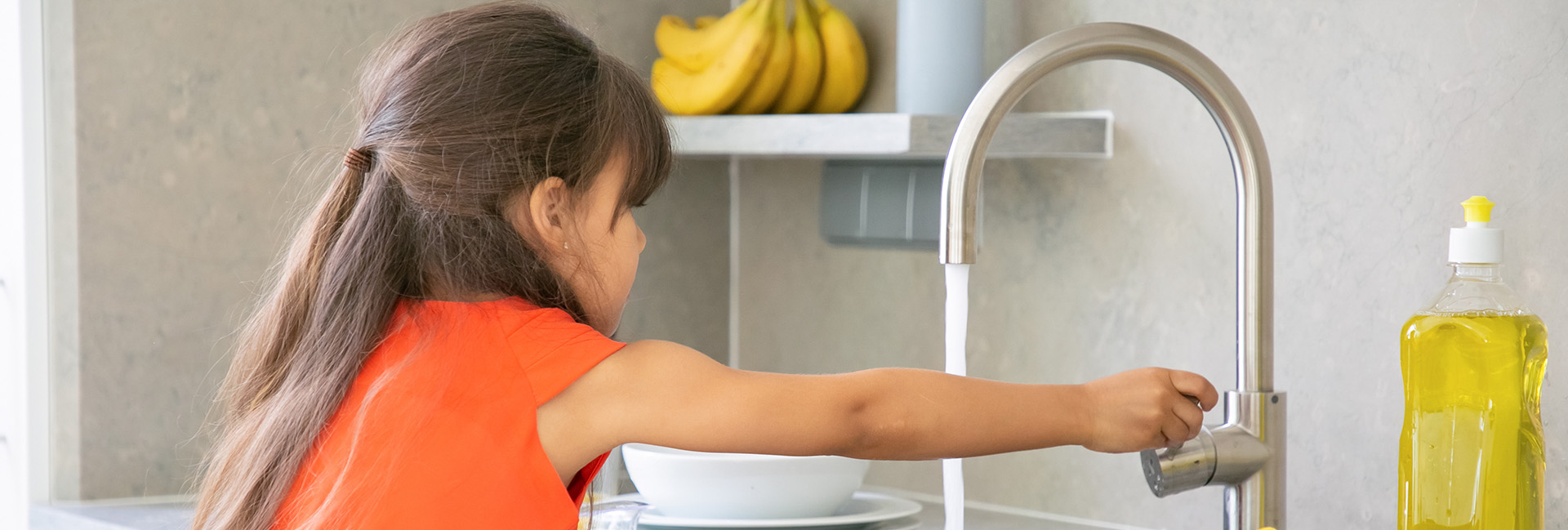 Cute little girl washing dish in kitchen by herself